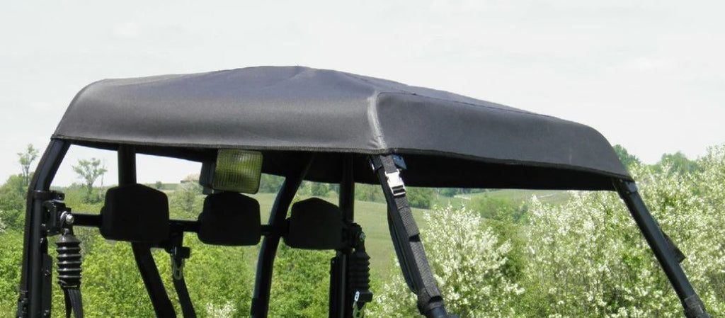 A close-up of the Arctic Cat Prowler 700 - Soft Top shows its black fabric canopy secured with straps on the roof, as the off-road vehicle sits outdoors surrounded by green trees beneath a cloudy sky.