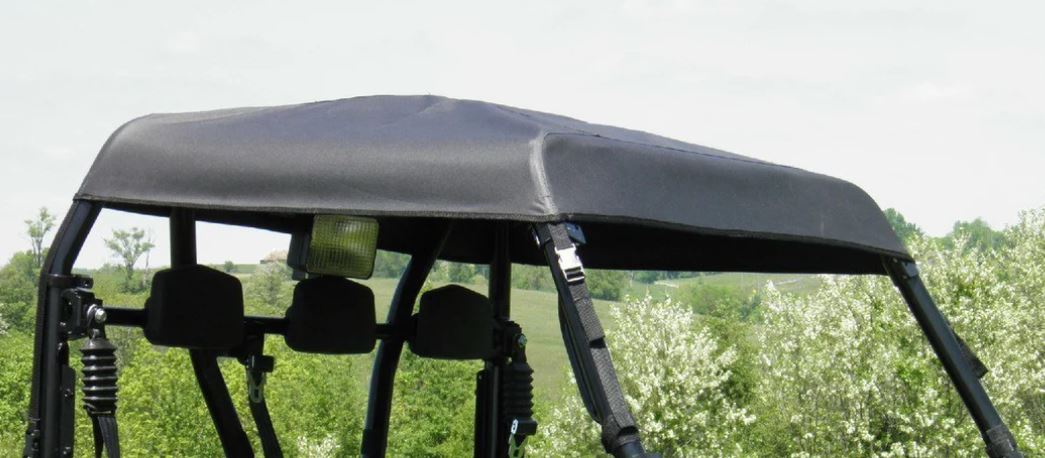 A close-up of the Arctic Cat Prowler 700 - Soft Top shows its black fabric canopy secured with straps on the roof, as the off-road vehicle sits outdoors surrounded by green trees beneath a cloudy sky.