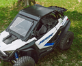 A Polaris RZR Pro XP with aluminum roof, blue suspension springs, tinted windshield, and blue RZR branding is parked on grass near a tree trunk.