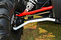 Close-up of the S3 Power Sports 2014+ Polaris Rzr Xp 1000 +2 Forward High Clearance A-Arm Kit installed, featuring a thick, deep-tread tire and bright red and white suspension arms on grassy terrain in daylight.