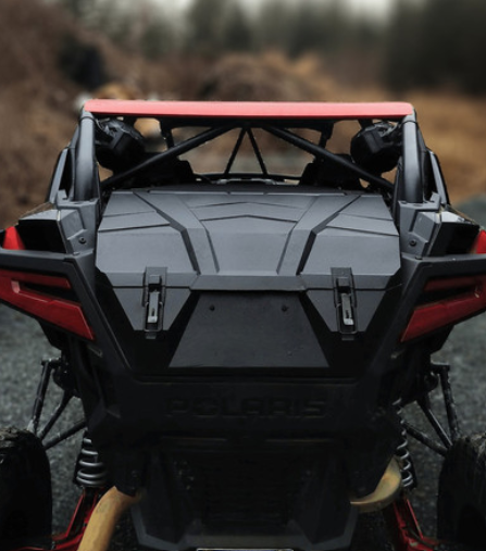 A rear close-up of the HIGHLANDS PXP Xtreme UTV Rear Cargo Box on a Polaris RZR Pro XP, showing its sleek angular design and robust build as it sits on a gravel path with blurred grass and trees in the background.