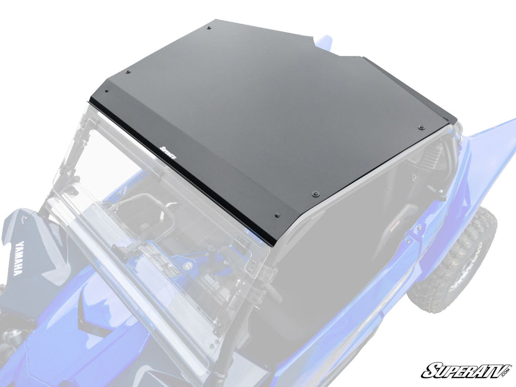 A Yamaha YXZ Aluminum Roof in matte black with visible bolts is installed on a bright blue Yamaha off-road vehicle, seen from above at an angle. The roof covers the open cabin, which has a clear windshield and minimal interior. SuperATV logo appears botto