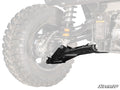 Close-up of Yamaha Wolverine X2 1000 High-Clearance Lower Rear A-Arms in black, installed on a rugged off-road vehicle. Large treaded tire and highlighted A-arm in foreground; rest of the vehicle is faded. SuperATV logo at bottom right.