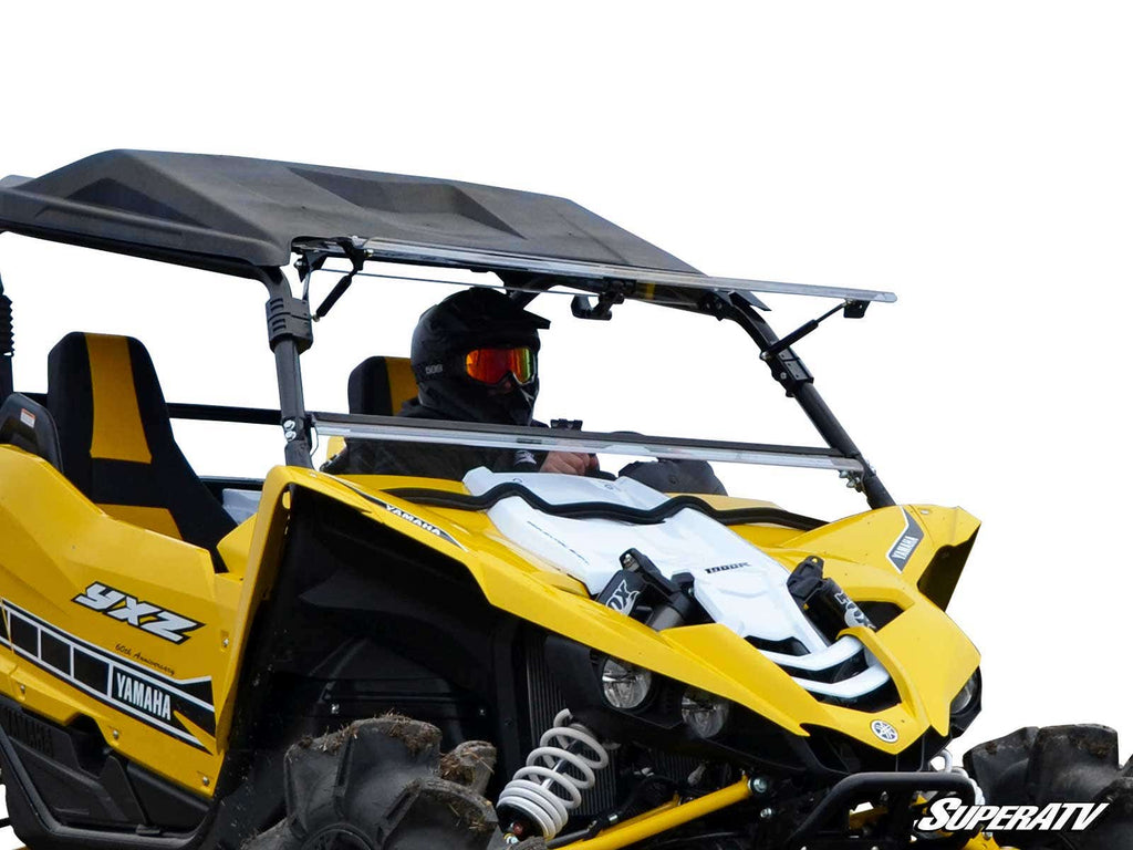 A person in a helmet and goggles drives a Yamaha YXZ with a Flip Windshield; only the upper section of the bright yellow side-by-side is visible against a white background.