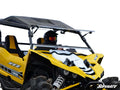 A person in a helmet and goggles drives a Yamaha YXZ with a Flip Windshield; only the upper section of the bright yellow side-by-side is visible against a white background.
