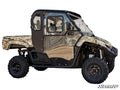 Side view of a Yamaha Viking with Convertible Cab Enclosure Doors, featuring a fully enclosed cabin, rugged off-road tires, black metal frame, and clear windows. The vehicle is on a white background with SuperATV branding in the bottom right.