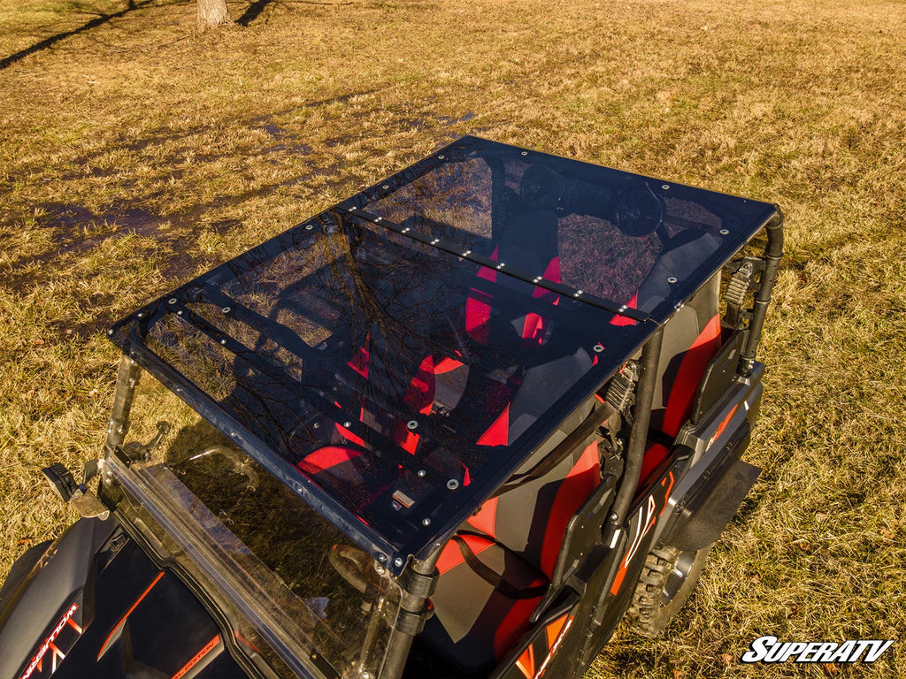 A Yamaha Wolverine X4 850 with a tinted polycarbonate roof is parked on dry grass; tree branches are reflected on the roof. The vehicle is red and black, features two seats, and the SuperATV logo appears in the lower right corner.